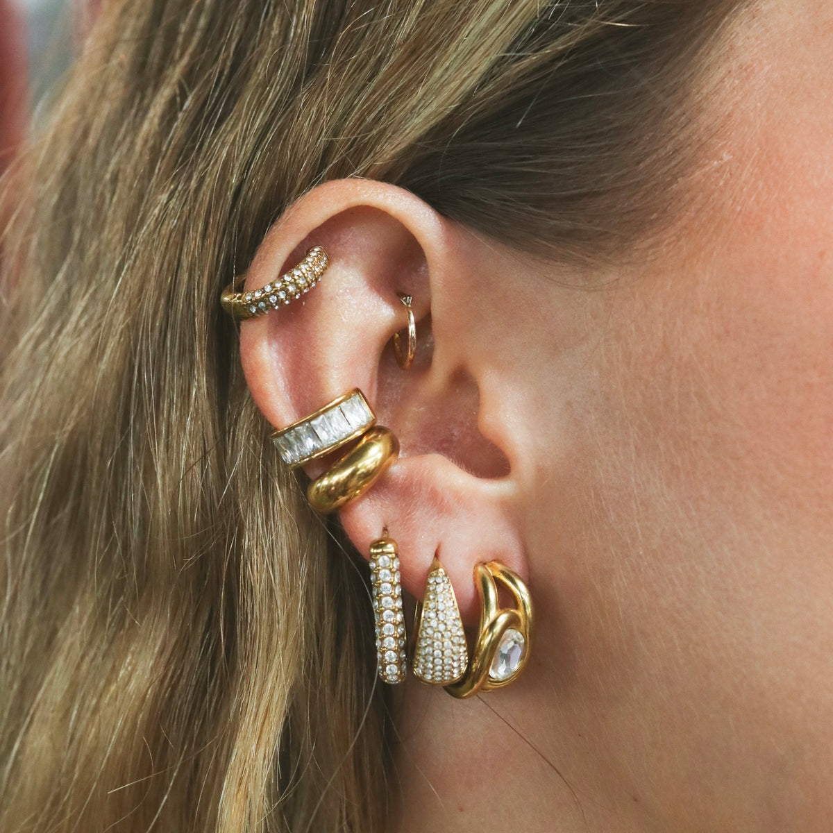 Oreille portant plusieurs bijoux dorés à pierres blanches, Rélia Bijoux